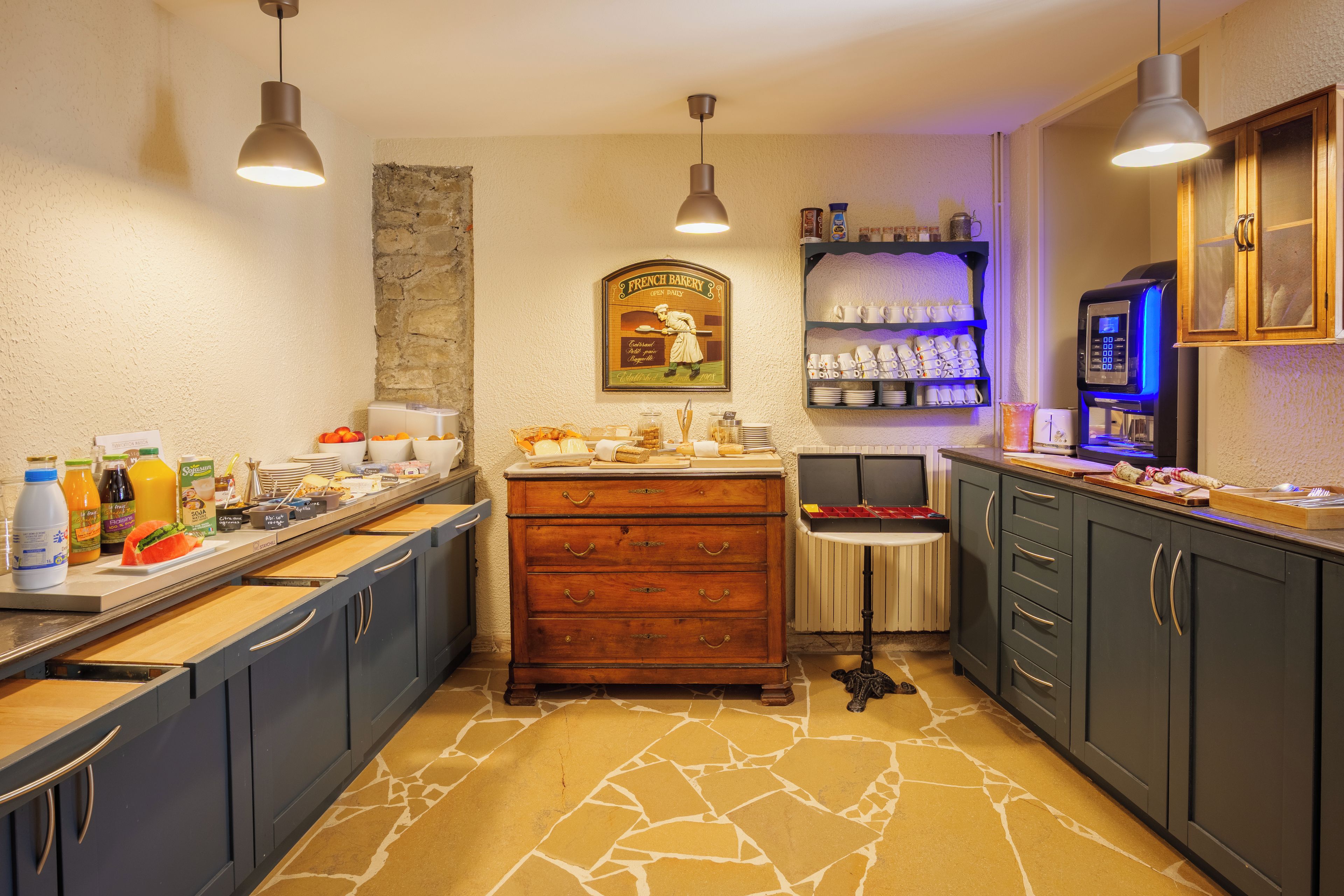 A kitchen with a stone-patterned floor, wooden cabinets, a coffee station, and a French bakery sign.