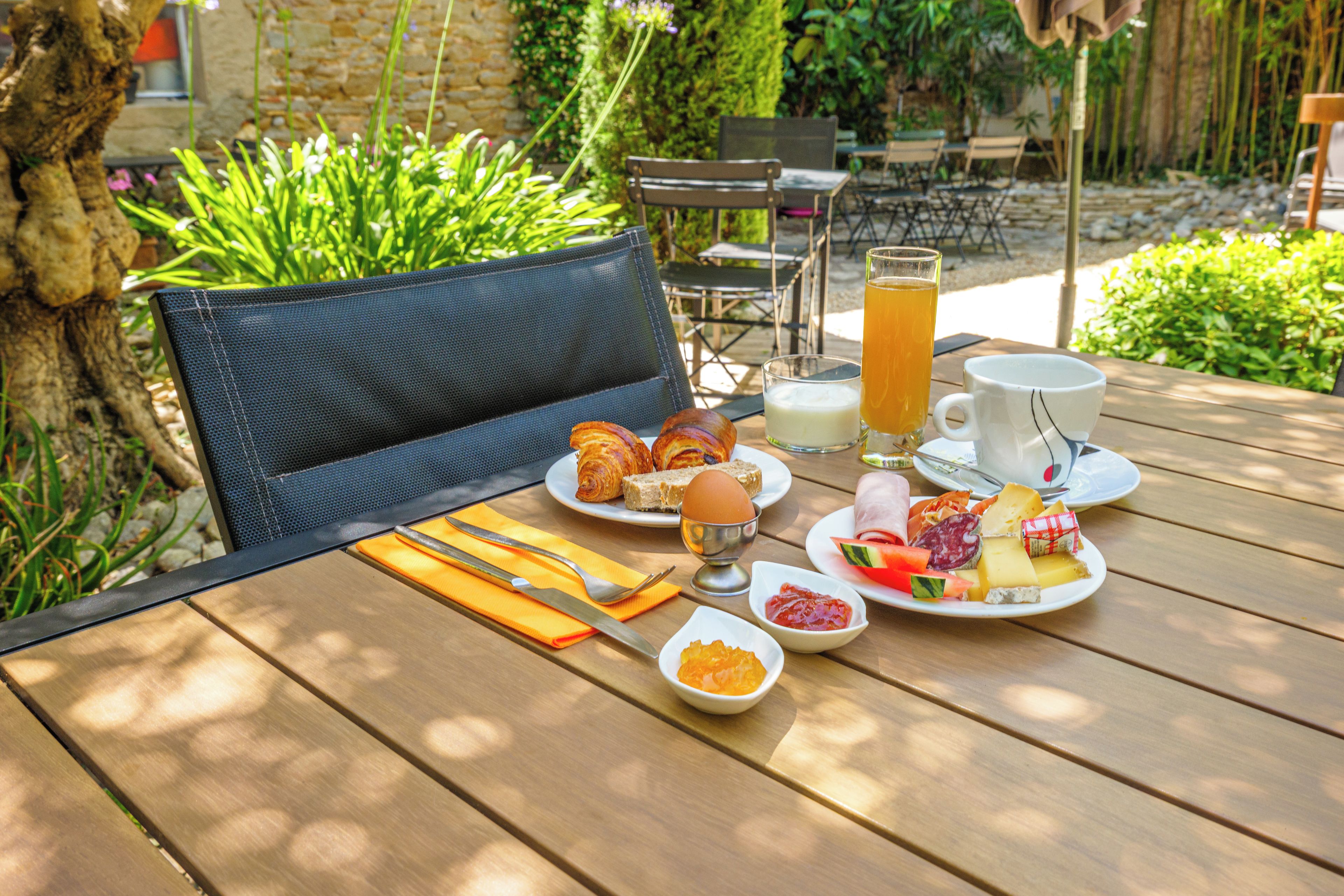 A wooden table set with breakfast items including croissants, eggs, cheese, and a glass of orange juice.