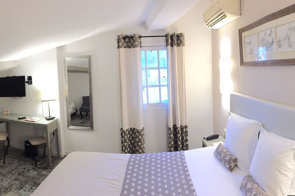 Une chambre d’hôtel de taille réduite, comprenant un lit, un bureau, une chaise, une télévision et une fenêtre avec des rideaux.