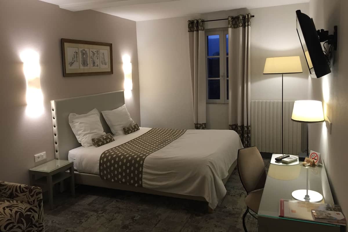 Une chambre d’hôtel comprenant un lit, une table de chevet, une chaise, un bureau, une lampe et un tableau au mur.