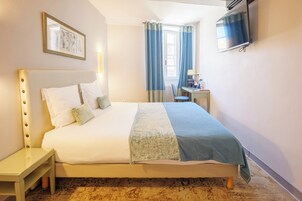 Una habitación de hotel con cama, escritorio, silla, televisor y ventana con cortinas.