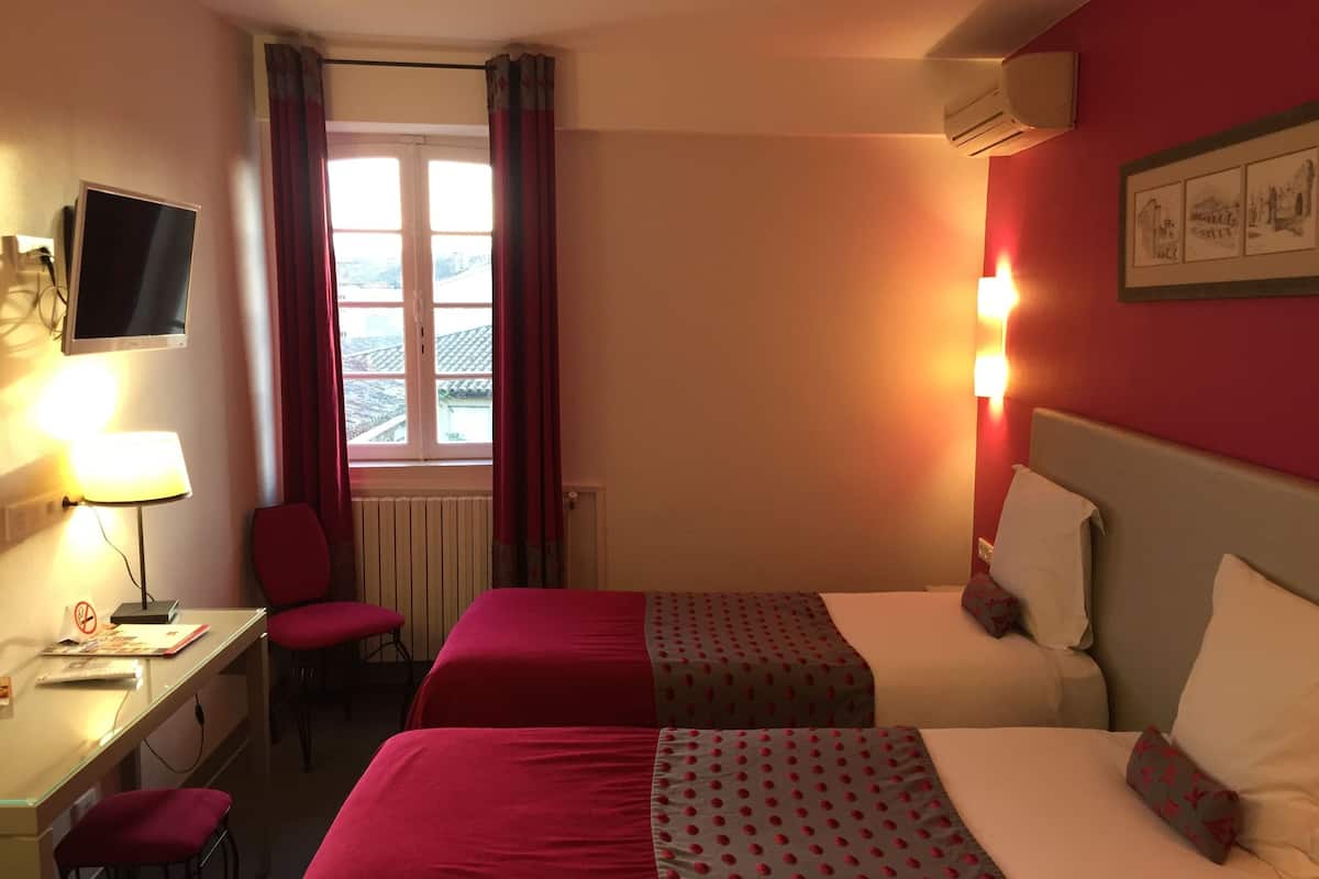Une chambre d’hôtel avec deux lits, un bureau avec une chaise, une télévision et une fenêtre avec des rideaux.