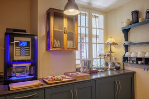 A kitchen with a coffee machine, a window with curtains, and various kitchen utensils on the counter.