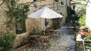 Un área de café al aire libre con suelo de piedra, mesas y sillas de madera, y faroles colgantes.