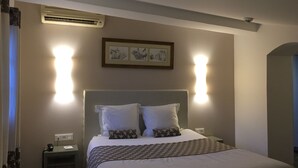 Habitación de hotel con cama, mesita de noche, lámpara, unidad de aire acondicionado y cuadro en la pared.