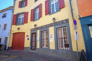 A hotel facade with a sign reading 'HOTEL DU PONT VIEUX,' featuring large windows with red shutters, a red door, and various posted signs including a no parking sign. - Hotel du Pont Vieux, au pied de la Cité Médiévale (Carcassonne)