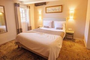 Habitación de hotel con una cama grande, dos mesitas de noche, un espejo, una ventana con cortinas y luces fijadas en la pared.