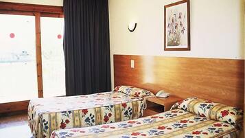 A hotel room with two beds, a wooden headboard, a bedside table with a phone, and a window with curtains.