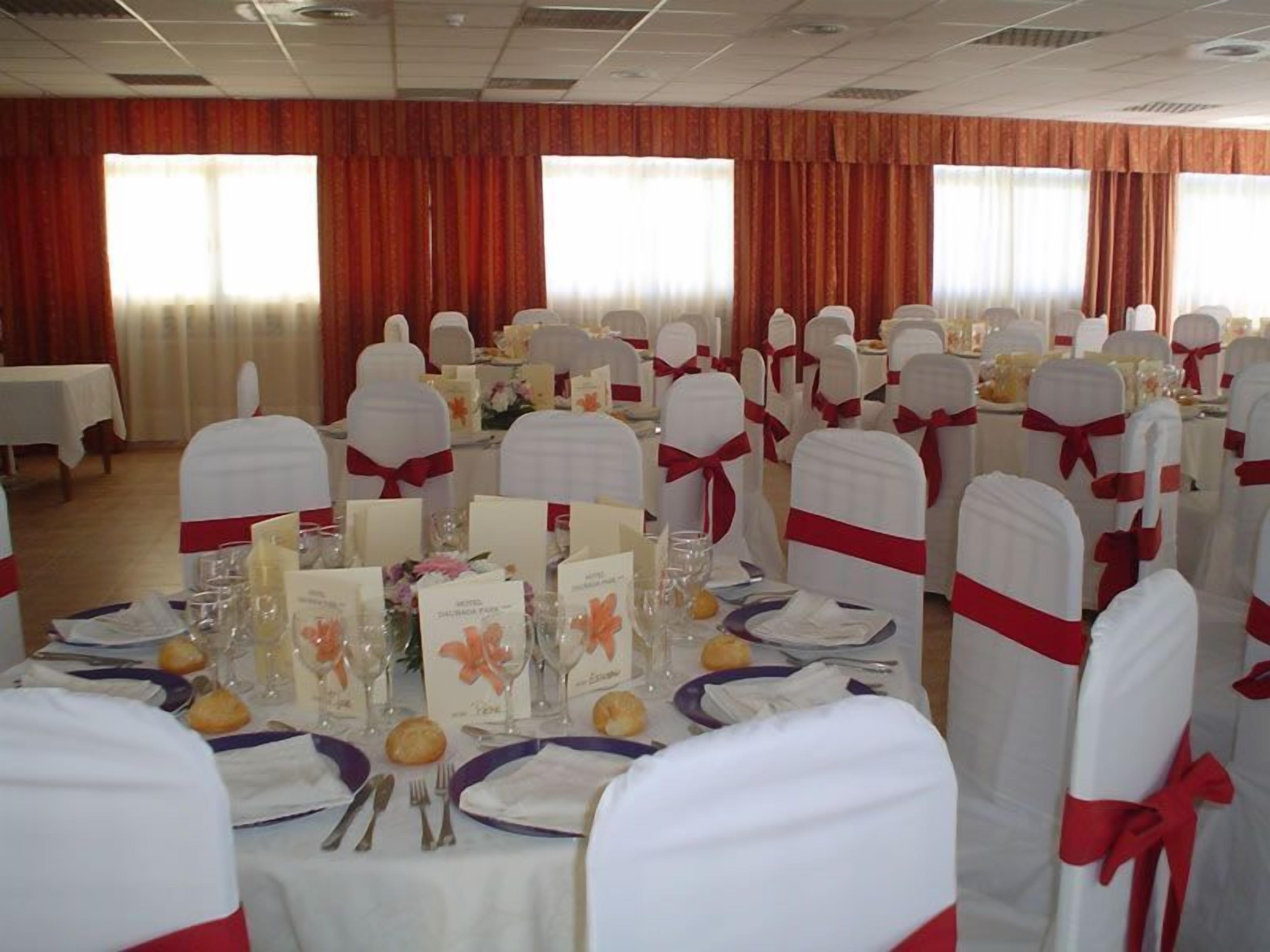 Une salle de banquet avec des tables rondes dressées pour un événement formel, agrémentée de nappes blanches, de rubans rouges et de centres de table floraux.