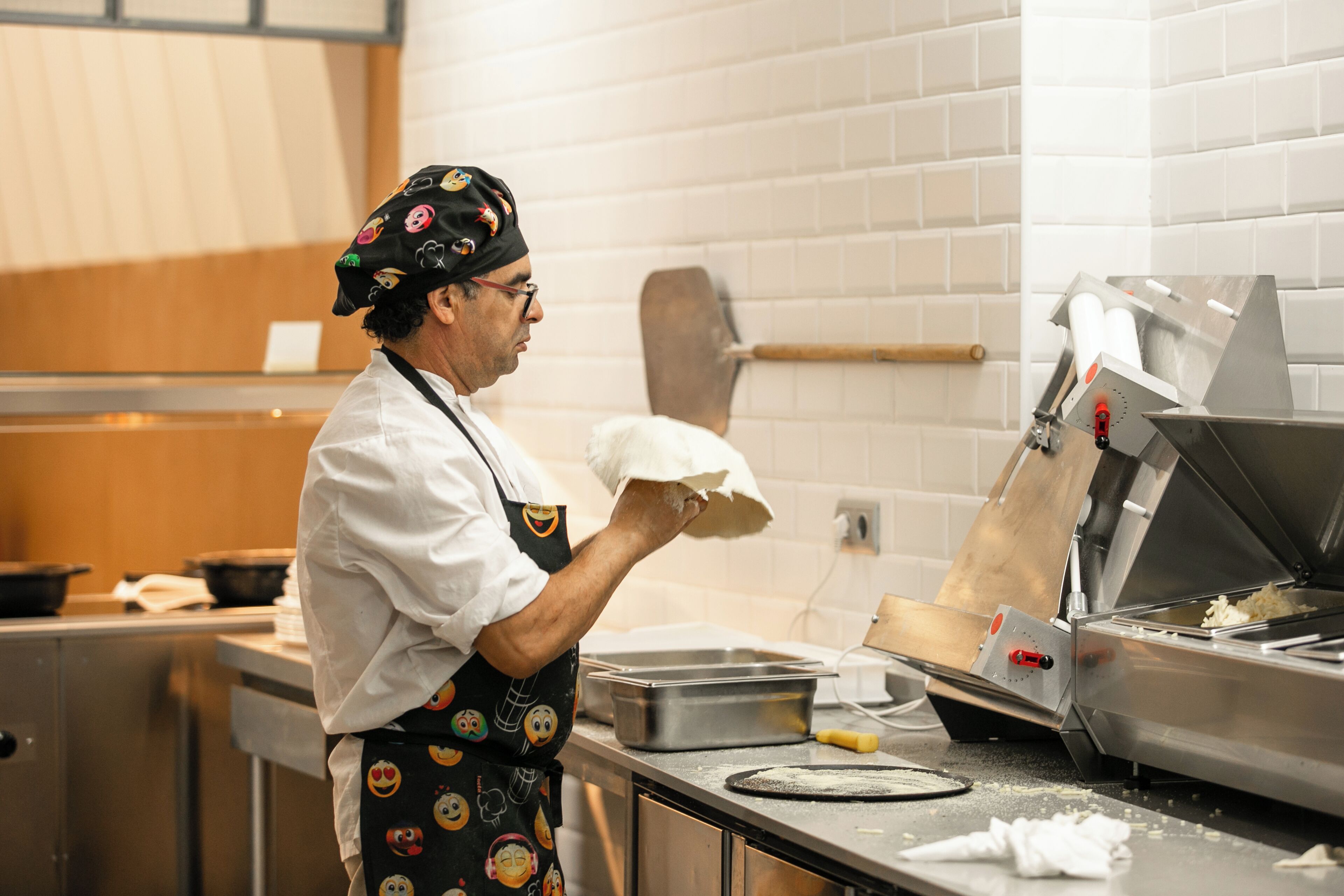 Een kok in een keuken met een bakstenen muur, een roestvrijstalen aanrecht en een groot contactrooster.