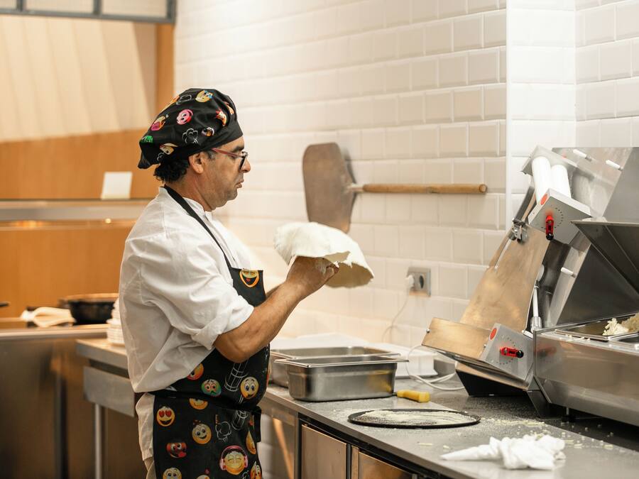 A chef in a kitchen with a brick wall, a stainless steel counter, and a large griddle.