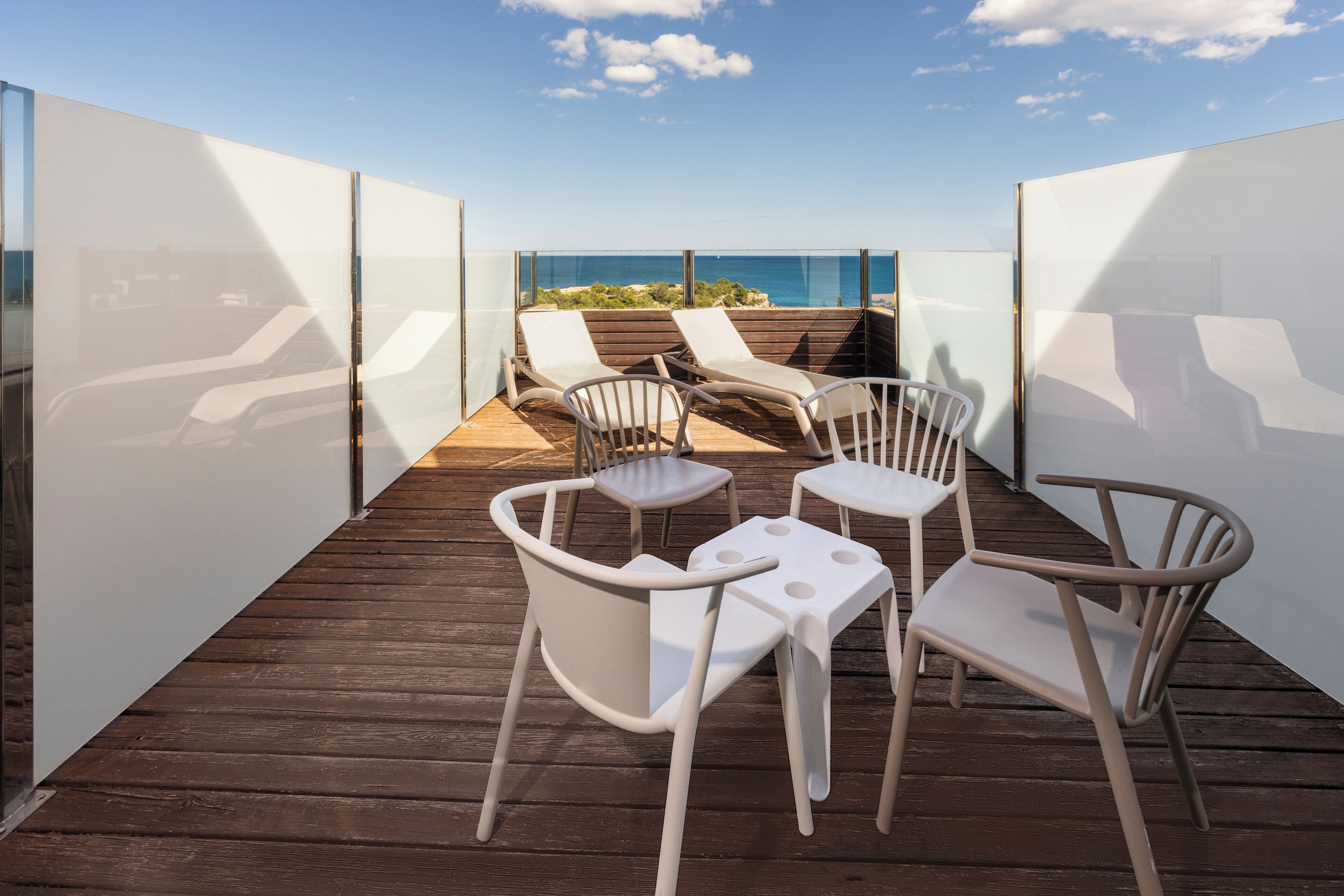 A deck with two lounge chairs and a small table, overlooking a beach.