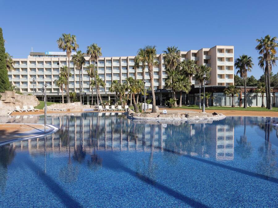 A hotel with a large pool, palm trees, and a clear blue sky.