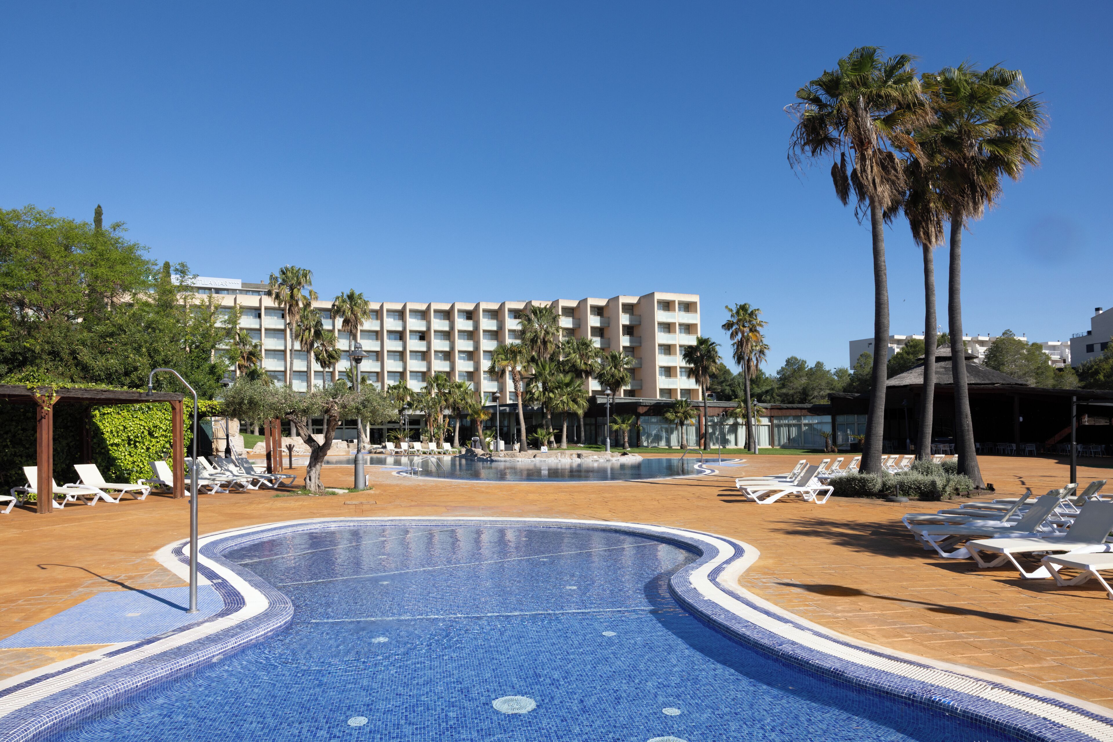 Ein Swimmingpool mit Liegestühlen, Palmen und einem Hotel im Hintergrund.
