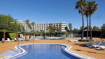 Ein Swimmingpool mit Liegestühlen, Palmen und einem Hotel im Hintergrund.