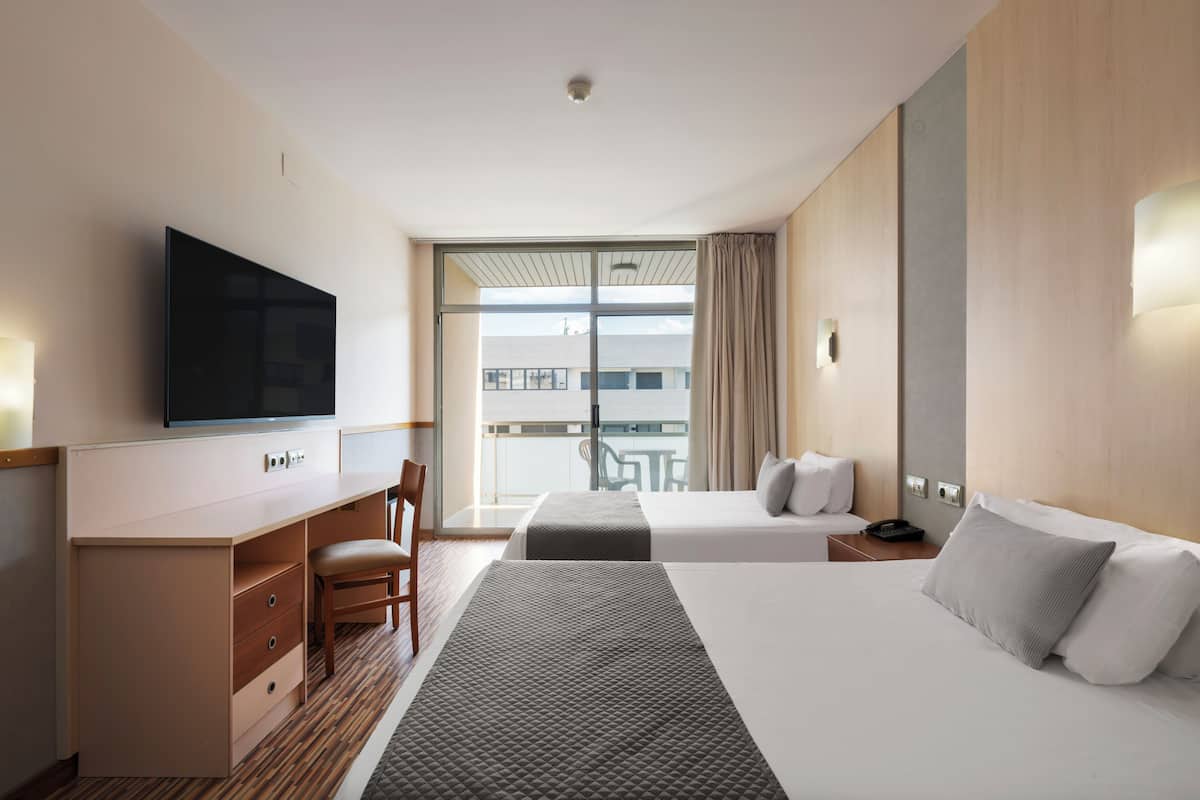 A hotel room with a bed, a desk, a chair, a television, and a balcony with a table and chairs.