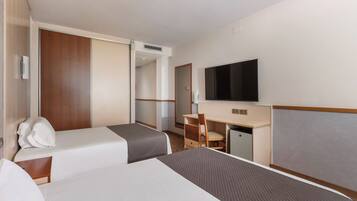 A hotel room with two beds, a desk, a chair, a television, and a wardrobe.
