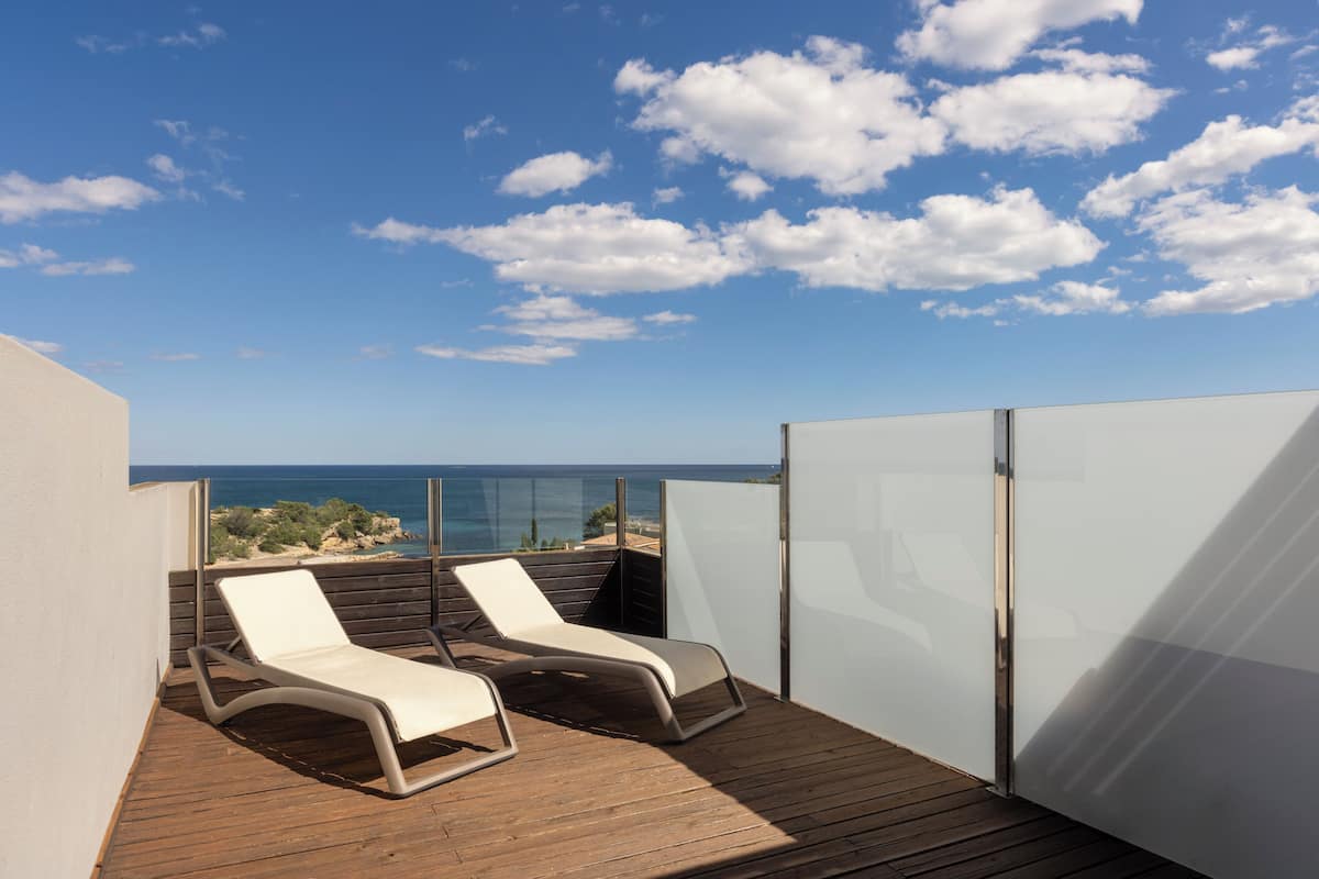 A balcony with two lounge chairs, a wooden deck, and a view of the sea.