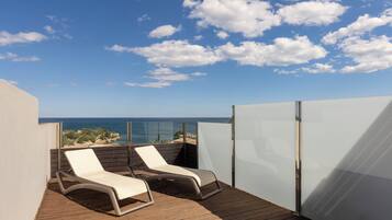 Un balcón con dos sillones de descanso, una terraza de madera y vista al mar.