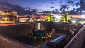 A rooftop terrace with a table and chairs, overlooking a cityscape at dusk. - Camelot Beach Suites (Clearwater Beach)