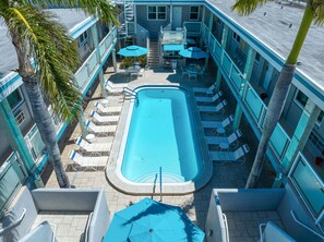 Un espace piscine doté de chaises longues et de parasols, entouré d’un bâtiment aux couleurs bleu et blanc.