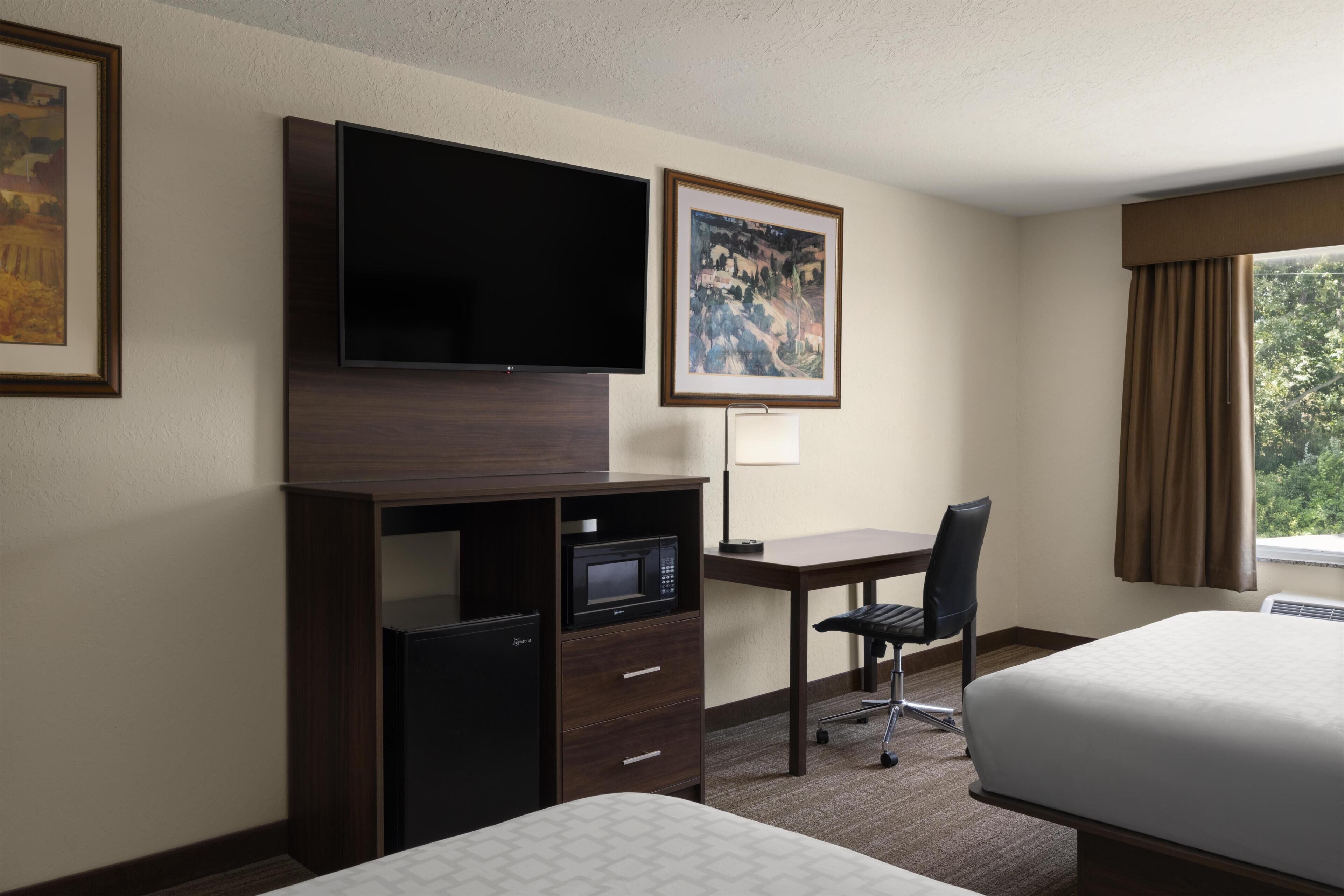 Una habitación de hotel con una cama, un escritorio con computadora, televisor, microondas y refrigerador pequeño.