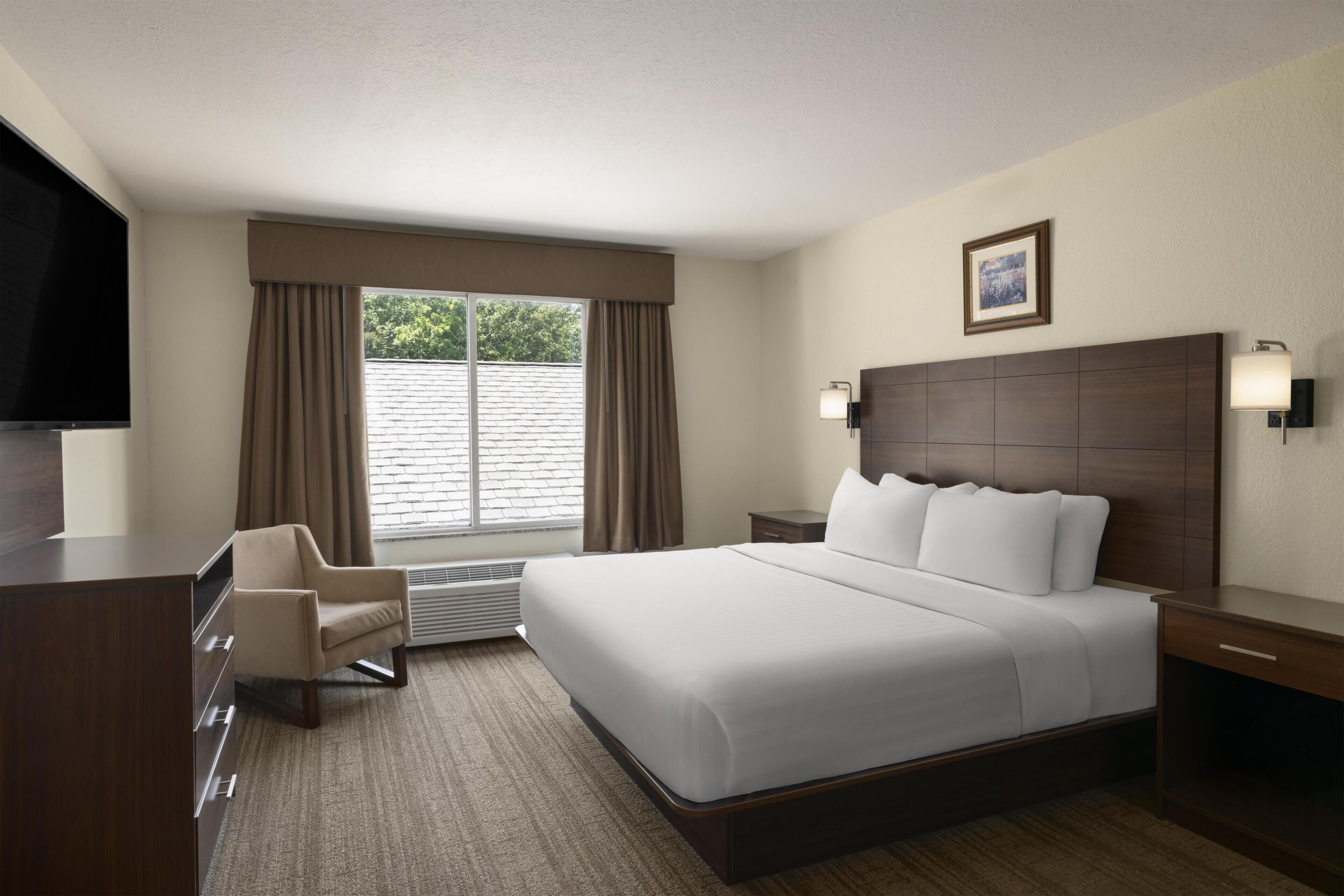 Habitación de hotel con una cama grande, un escritorio, una silla, un televisor y una ventana con cortinas.