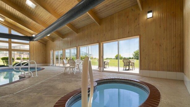 An indoor swimming pool with a brick border, wooden walls, and a view of the outdoors.