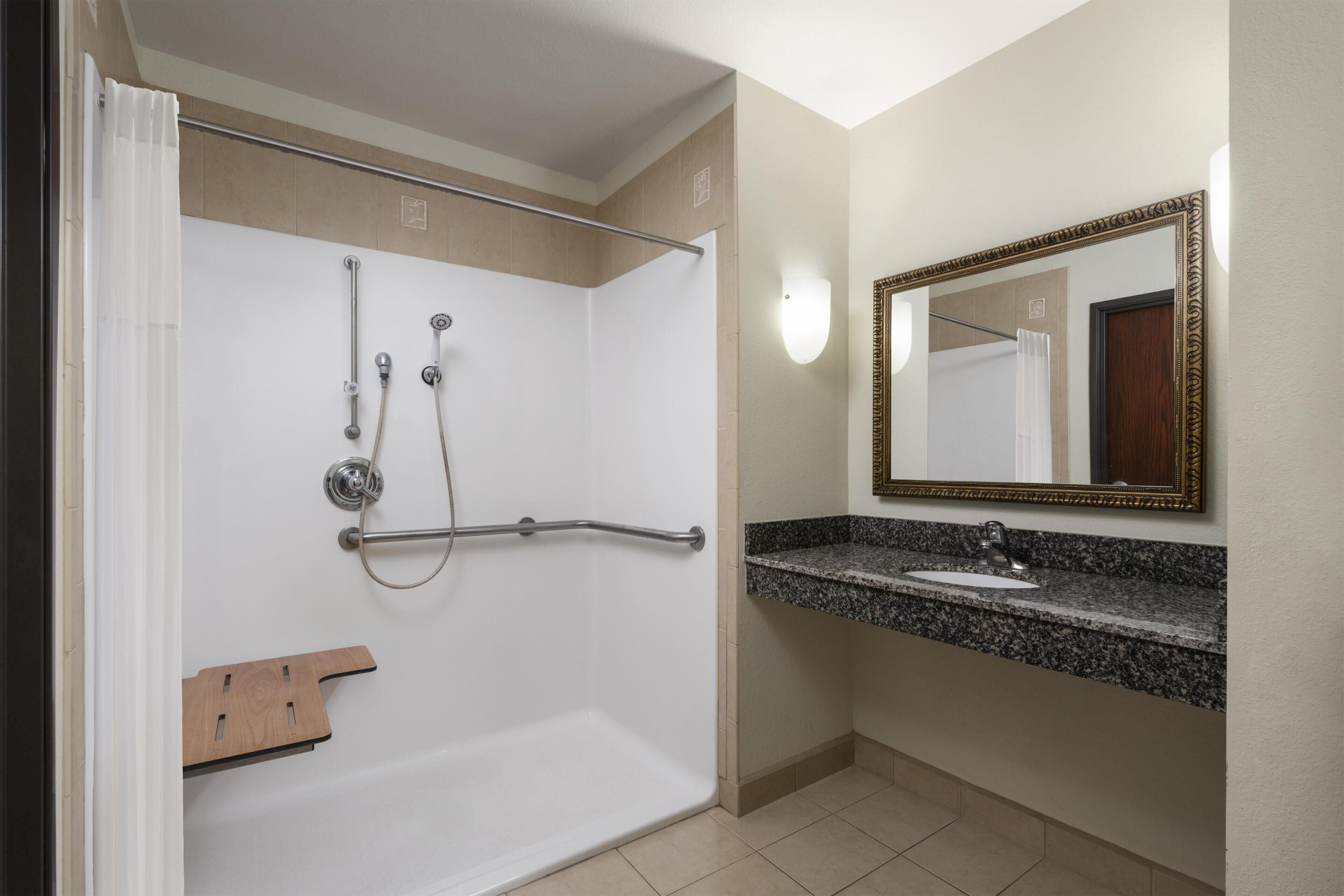 A bathroom with a shower, a sink, a mirror, and a towel rack.
