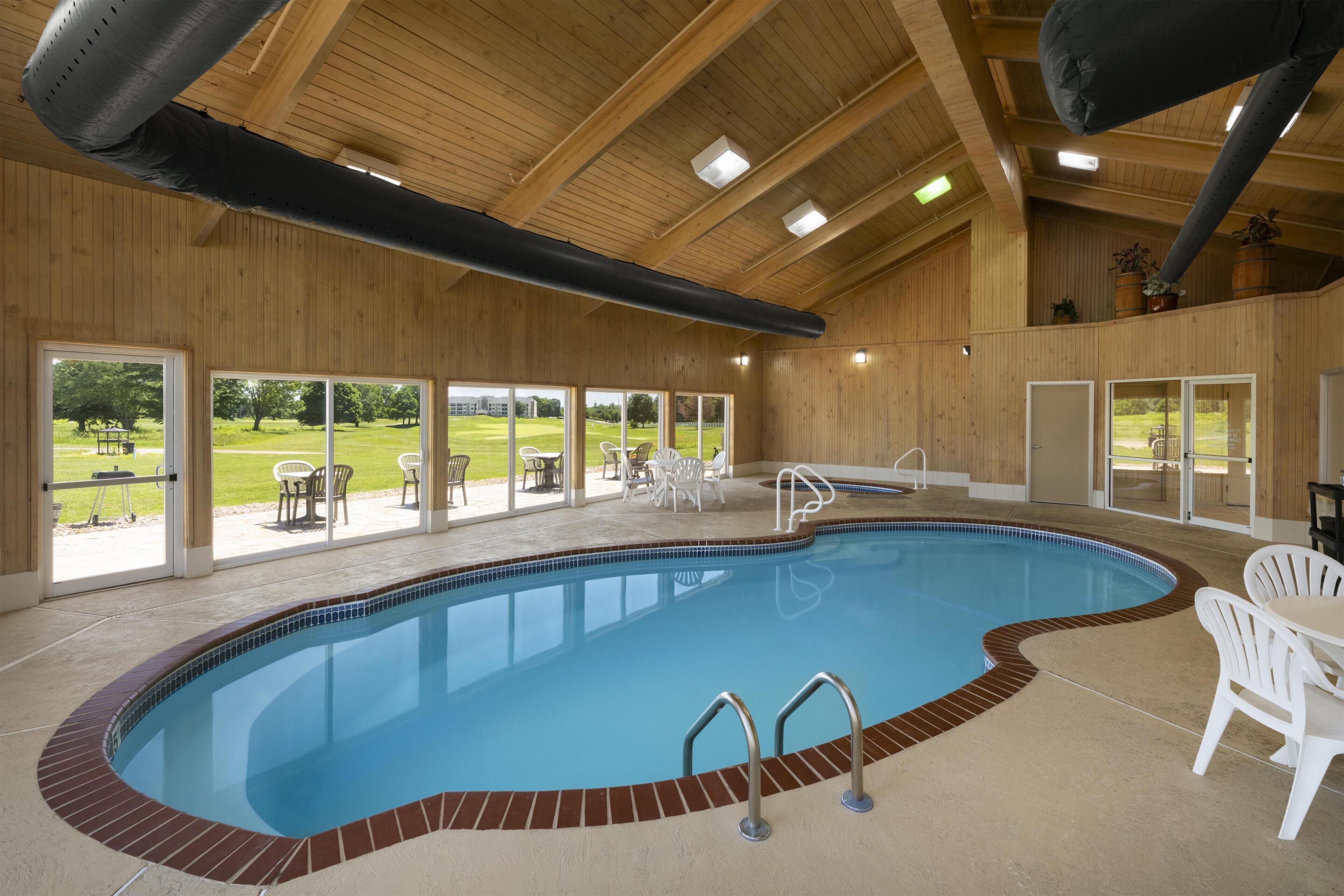 Una piscina interior con techo de madera, puertas de cristal transparente y zona de estar exterior.