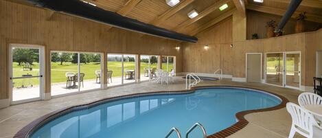 Une piscine intérieure dotée d’un plafond en bois, de portes en verre transparent et d’un espace extérieur aménagé pour s’asseoir.