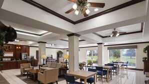 A spacious hotel lobby with a dining area, kitchen, and large windows.