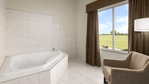 A modern bathroom with a bathtub, a window with curtains, and a view of a green landscape.