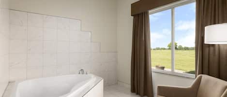 A modern bathroom with a bathtub, a window with curtains, and a view of a green landscape.