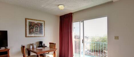 Ein Hotelzimmer mit Bett, Schreibtisch mit Stuhl, Fernseher, einem Bild an der Wand und einem Balkon mit Aussicht.