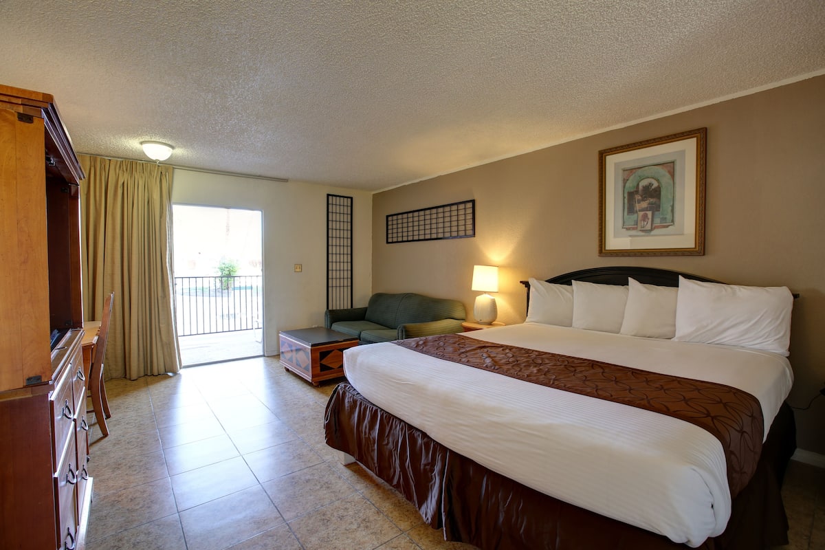 A hotel room with a large bed, a sofa, a desk, and a view of the outdoors.
