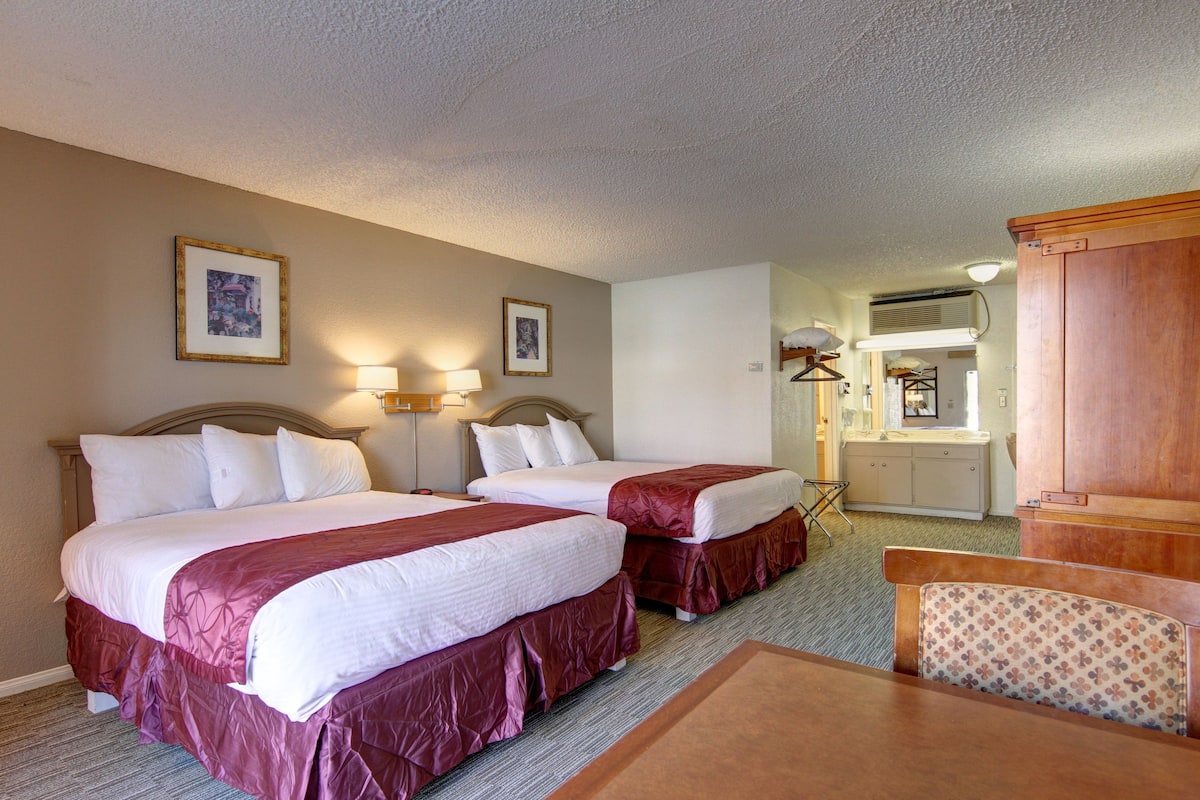 A hotel room with two beds, a wooden headboard, a desk, and a chair.