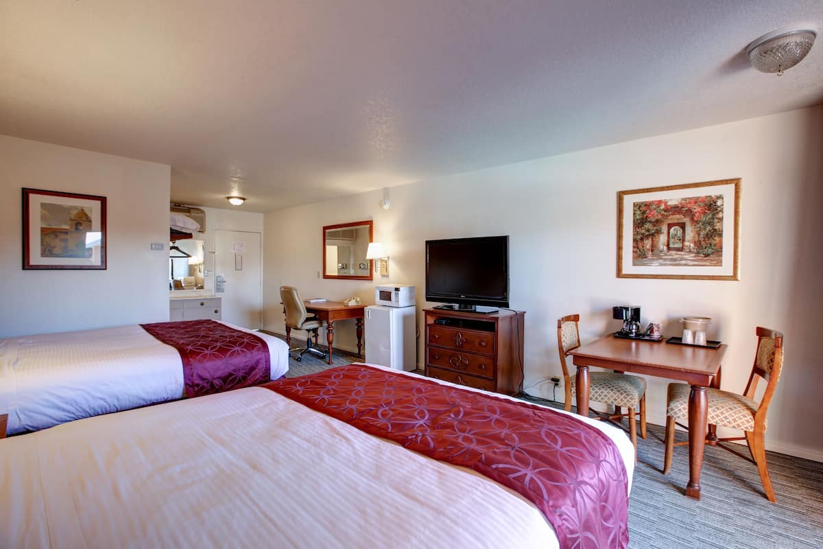 A hotel room with two beds, a desk, a television, a chair, and a dining table.