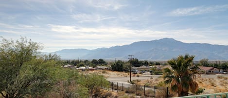 A view from a balcony overlooking a desert landscape with mountains in the distance, a road, and sparse vegetation.