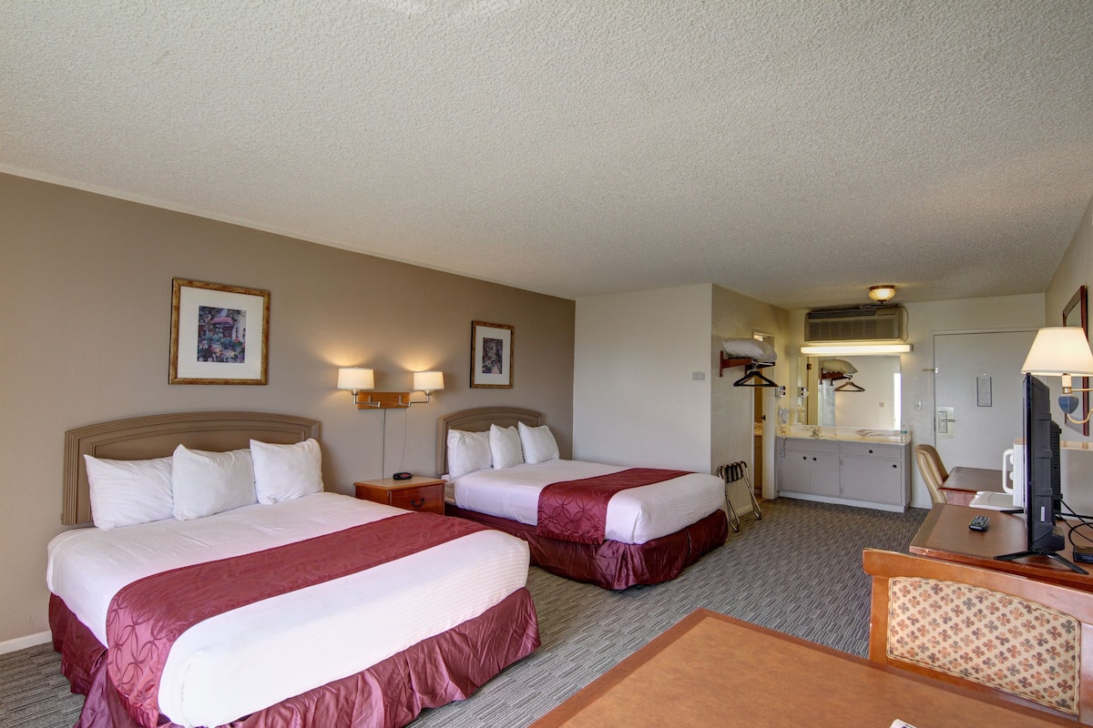 A hotel room with two beds, a desk with a computer, a chair, and a small kitchenette.
