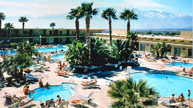 A resort with multiple swimming pools, palm trees, and a mountain backdrop.