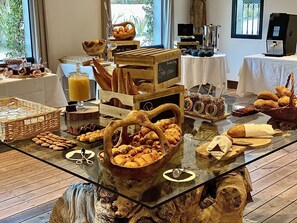 A breakfast buffet with various pastries, bread, and beverages on a glass table with wooden accents. - Le Roi Théodore (Porto-Vecchio)