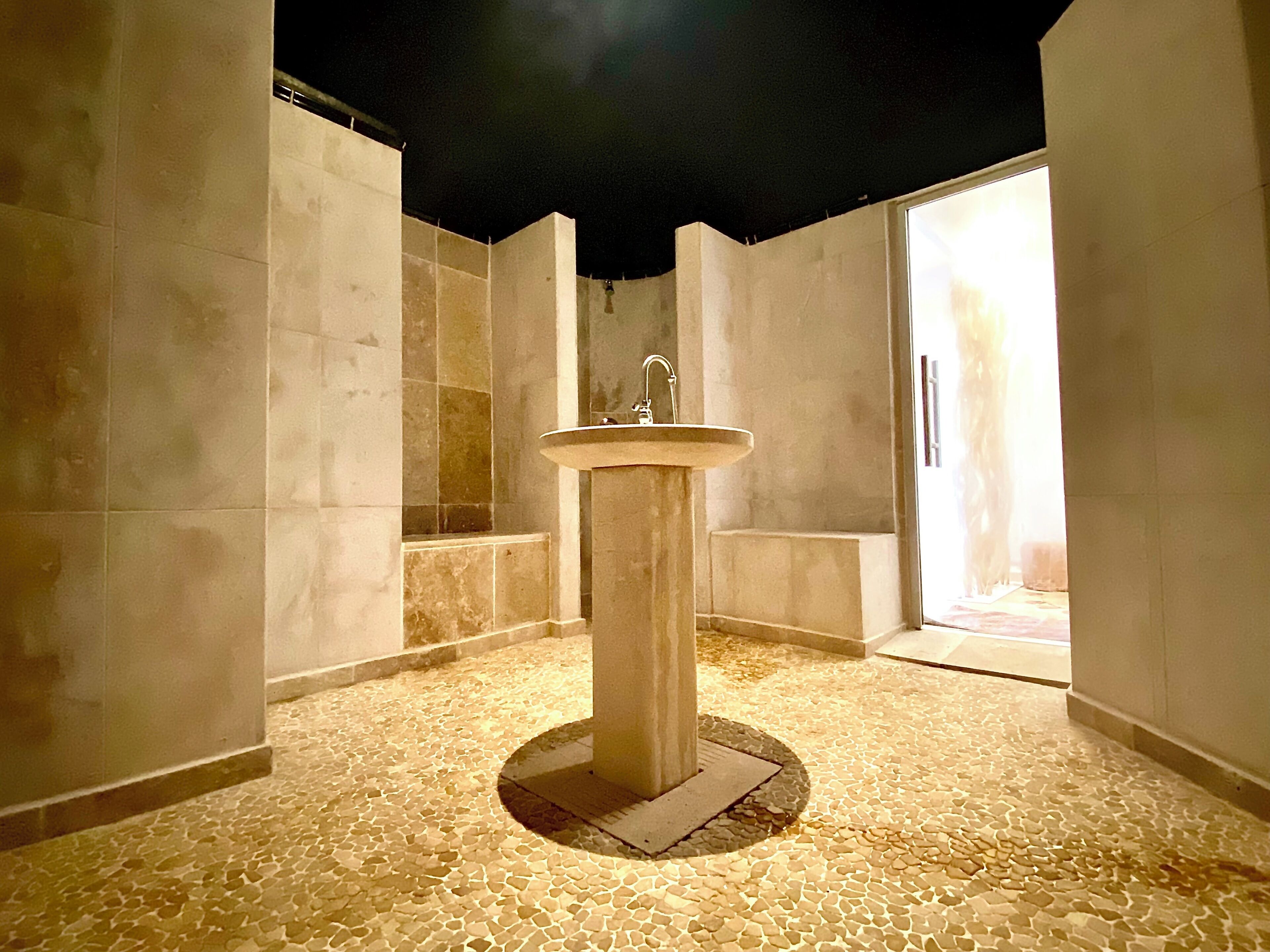 A bathroom with a central sink, tiled walls, and a stone-patterned floor.