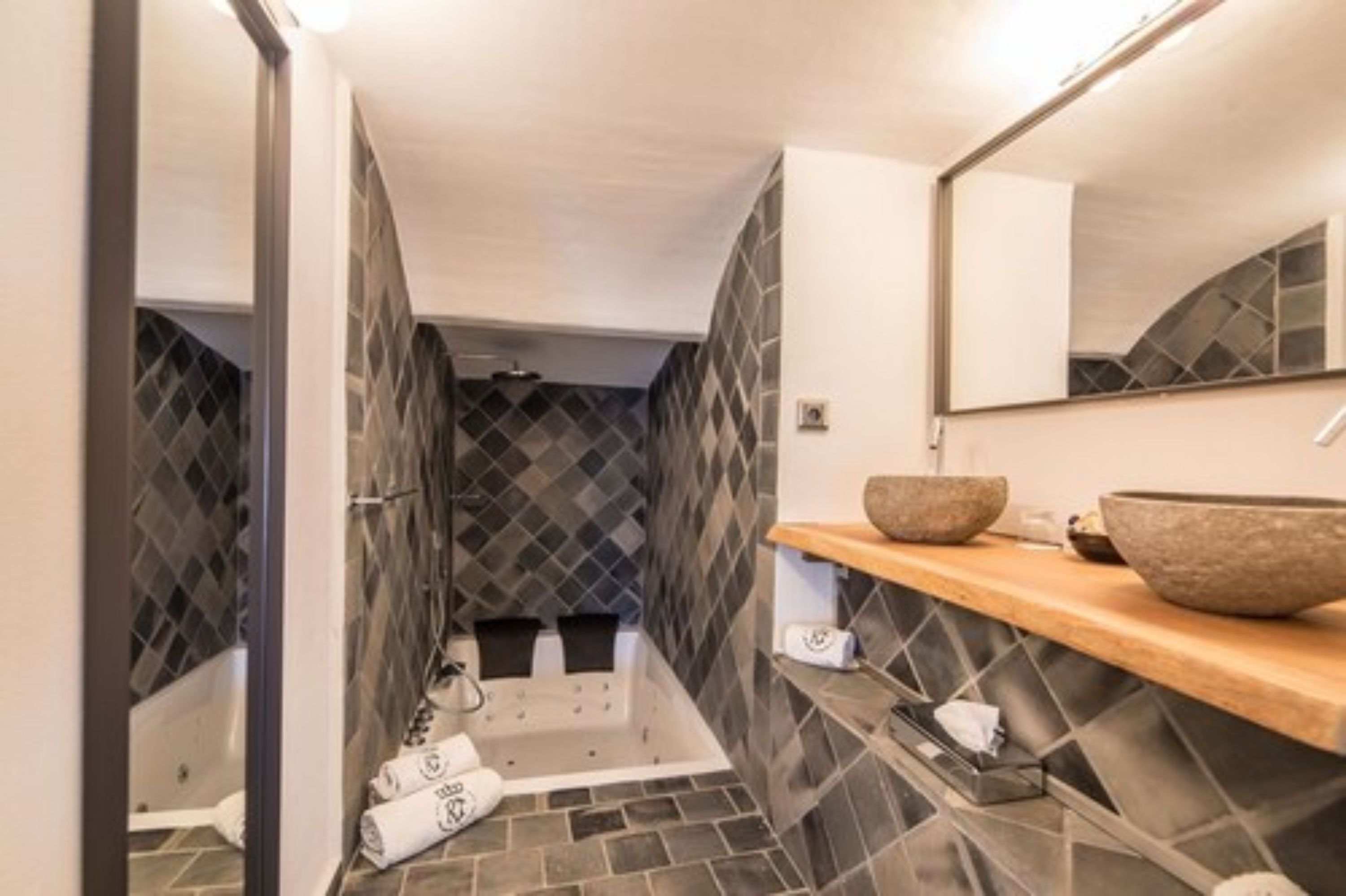 A modern bathroom with a bathtub, a large mirror, and a wooden shelf with a stone basin.