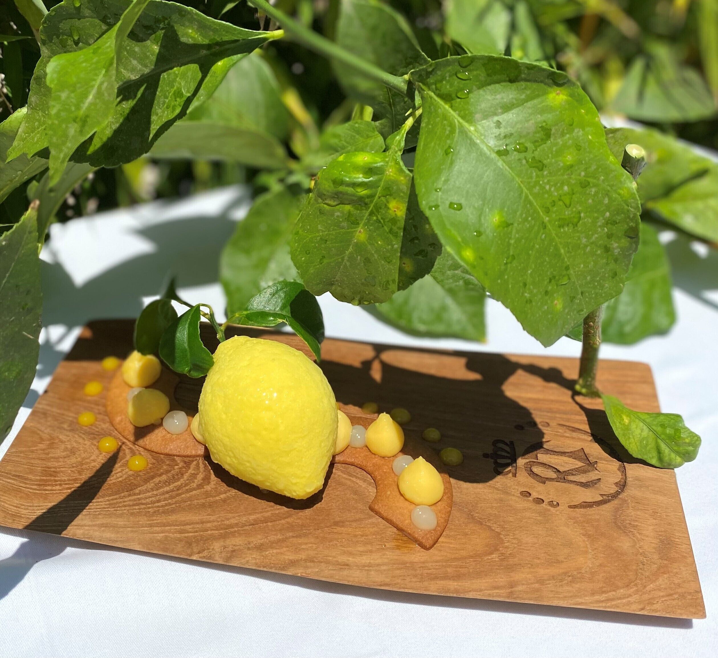 Una tabla de madera con un limón y objetos amarillos pequeños sobre una superficie blanca.