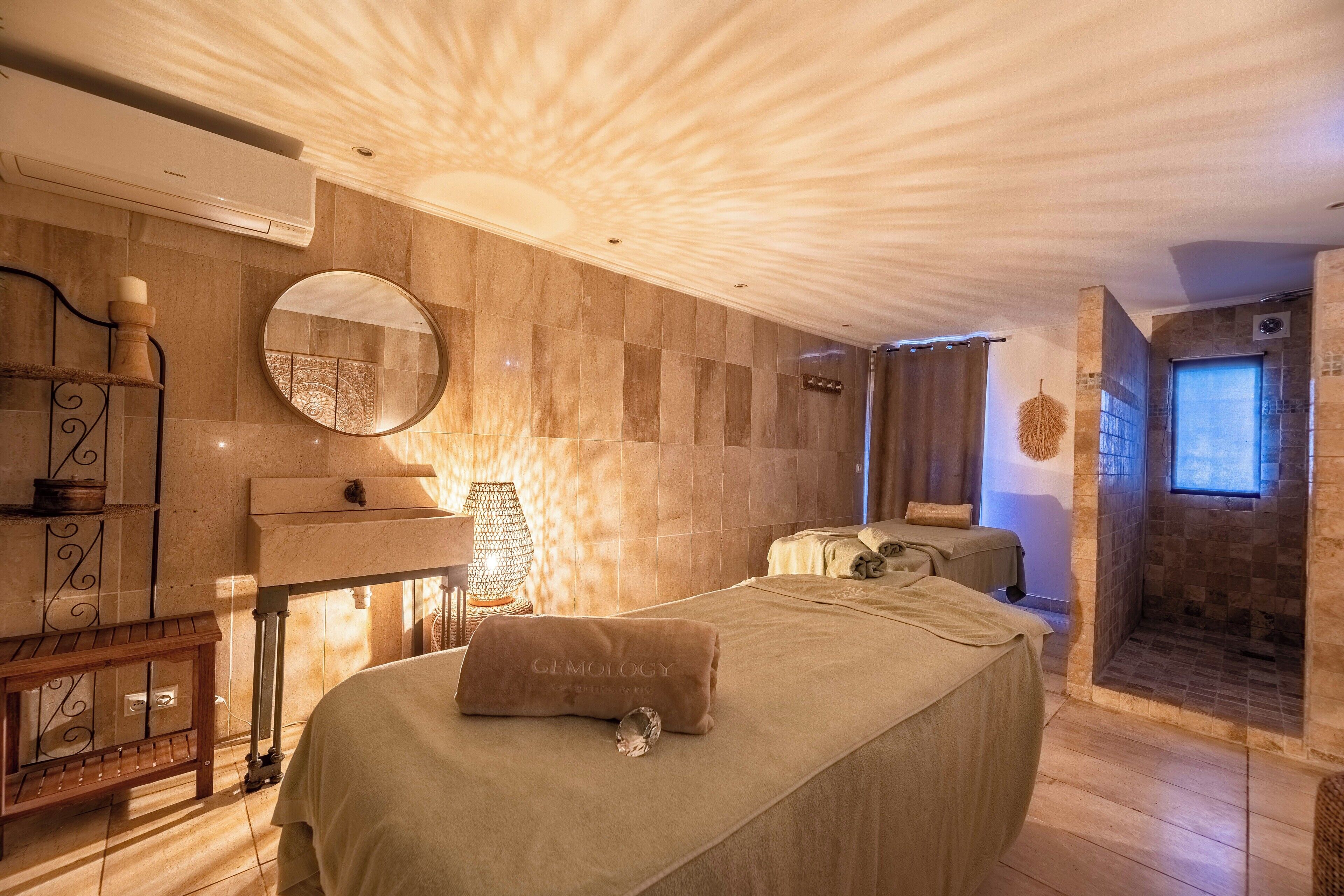 Une salle de spa équipée d’un lit, d’un miroir, d’une étagère fixée au mur, d’une lampe décorative et d’un espace douche.