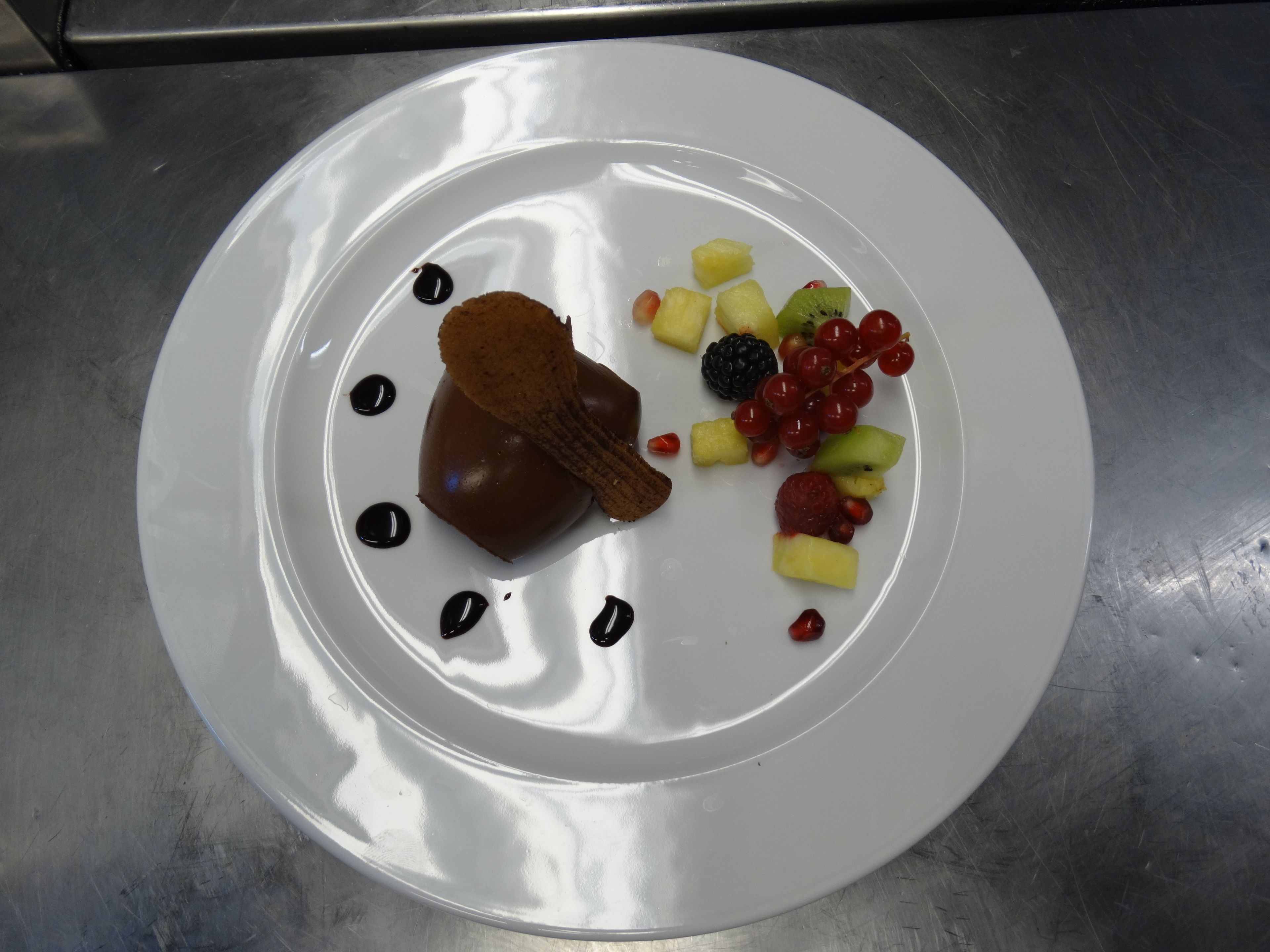 A white plate with a dessert, including a chocolate heart-shaped item, and various fruits like strawberries, blackberries, and grapes.