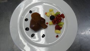 A white plate with a dessert, including a chocolate heart-shaped item, and various fruits like strawberries, blackberries, and grapes.