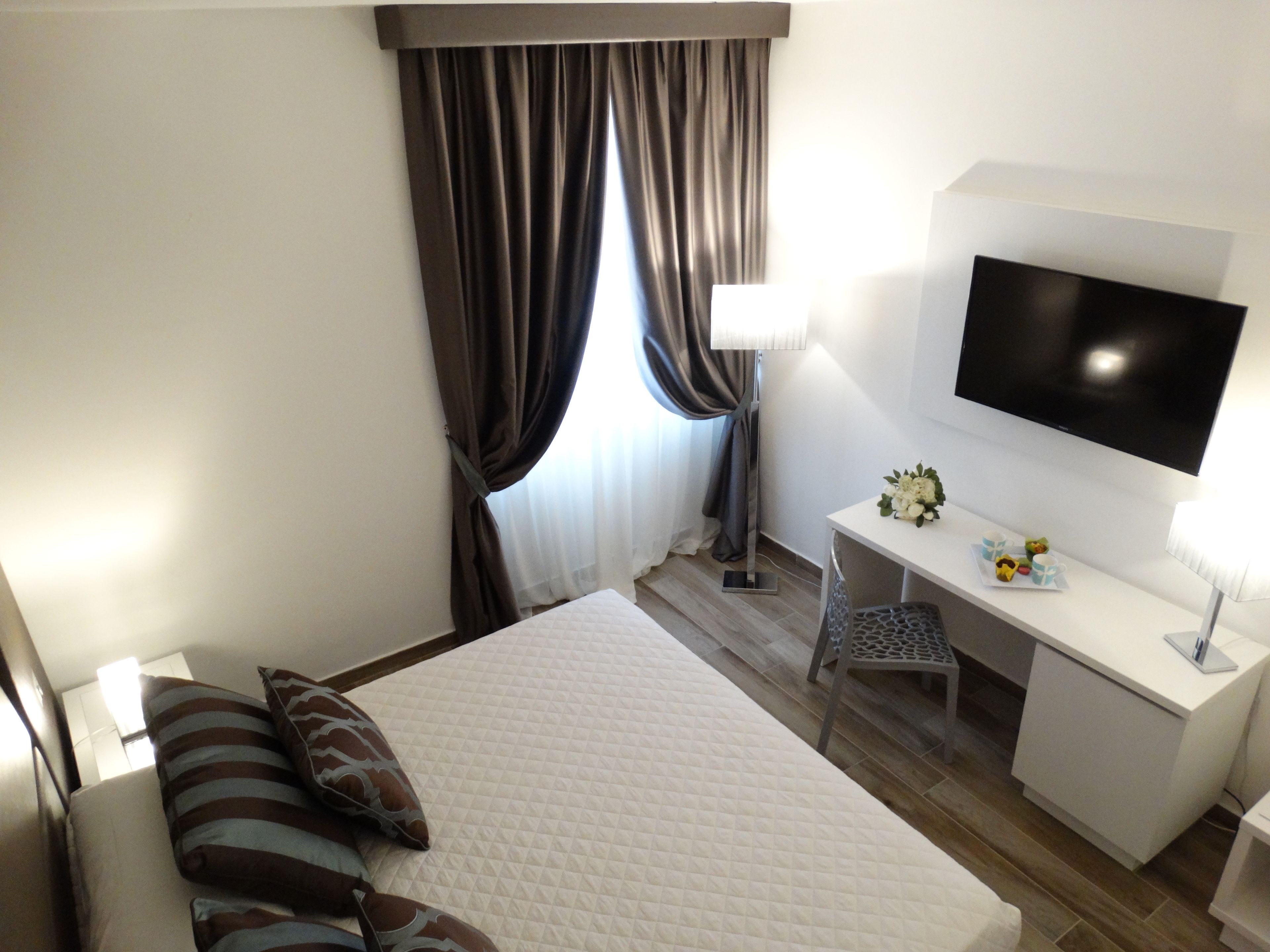 Una habitación de hotel con cama, escritorio, silla, televisión y ventana con cortinas.