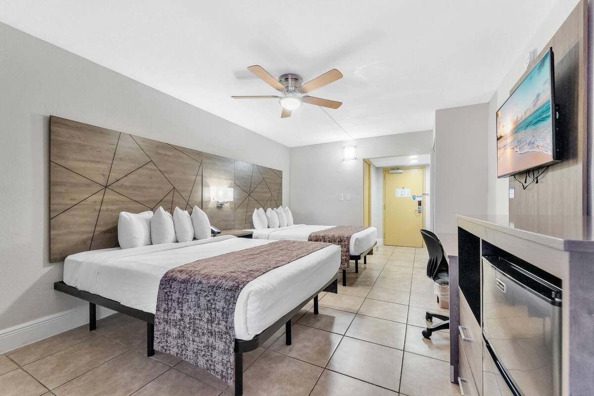 Een hotelkamer met twee bedden, een plafondventilator, een televisie, een bureau en een koelkast.